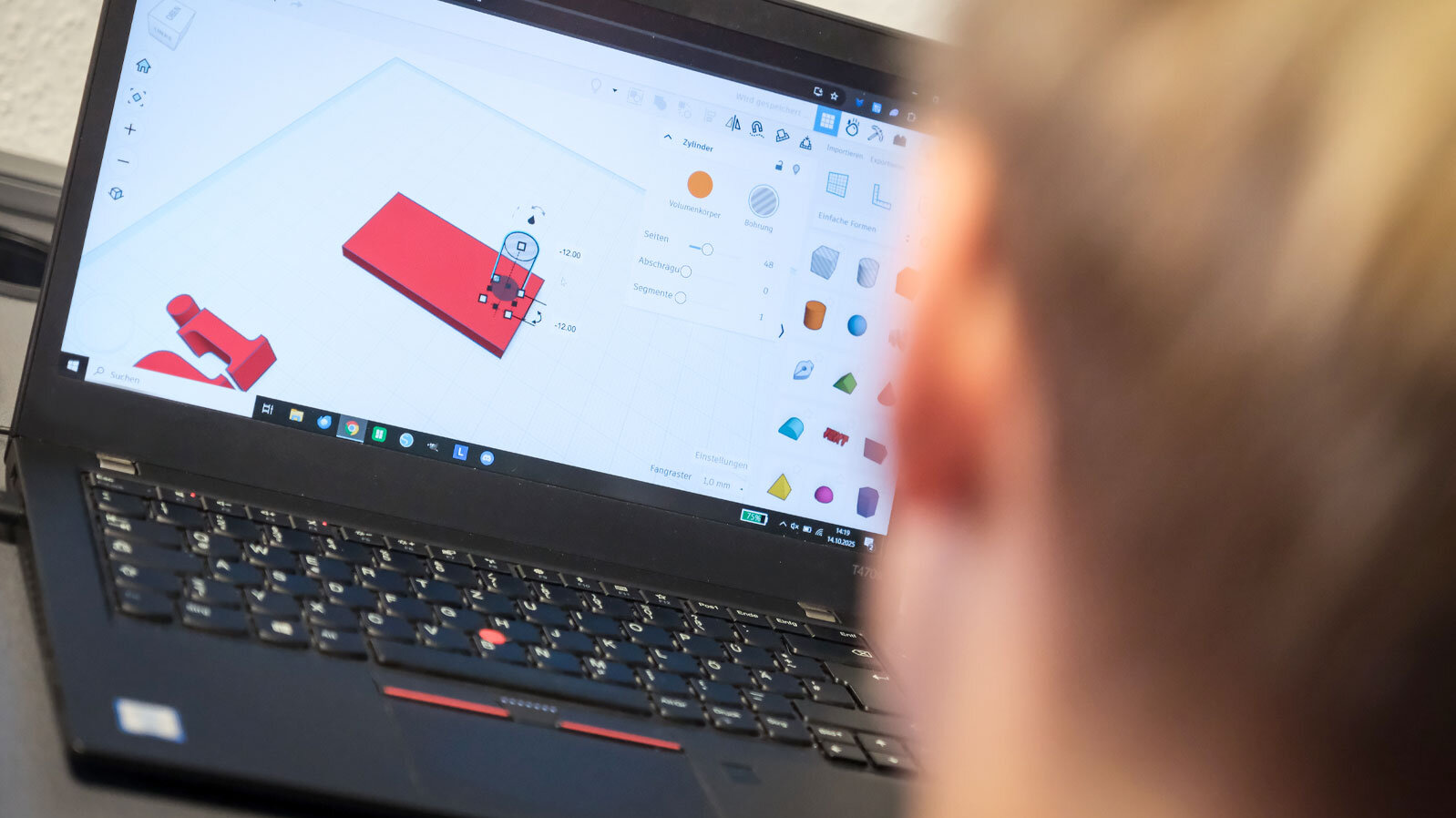 Ein Junge sitzt vor einem Computer und platziert in einem Programm Zylinderformen auf einer Farbfläche
